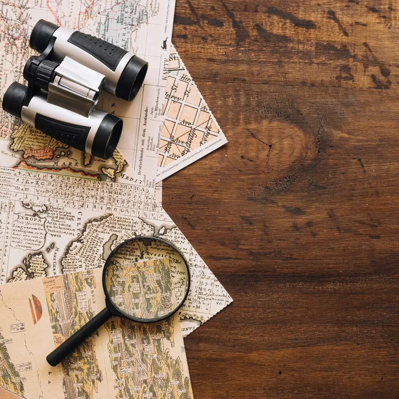 Nahaufnahme einer Lupe und eines Fernglases auf Landkarten.